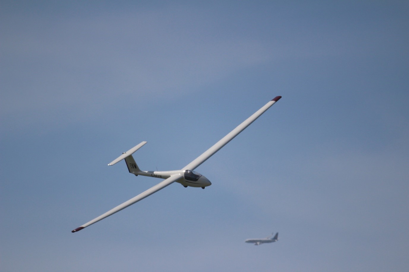 A glider with a commercial aircraft flying in the distance