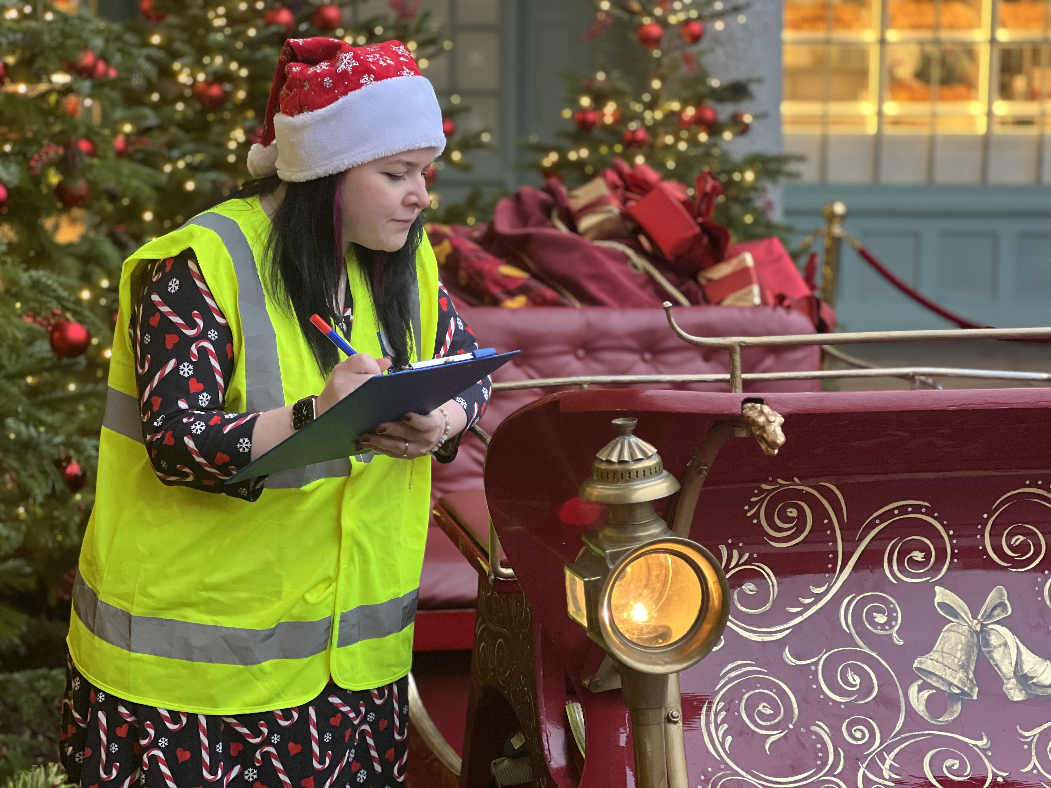 Woman (left), holding clipboard inspecting red sleigh.