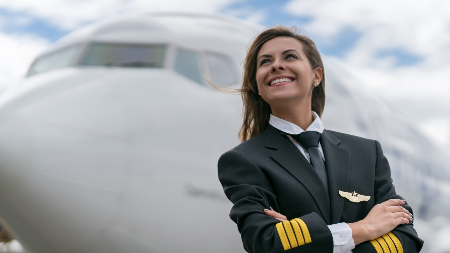 An image of a female pilot with crossed arms smilling in front of a commercial aircraft